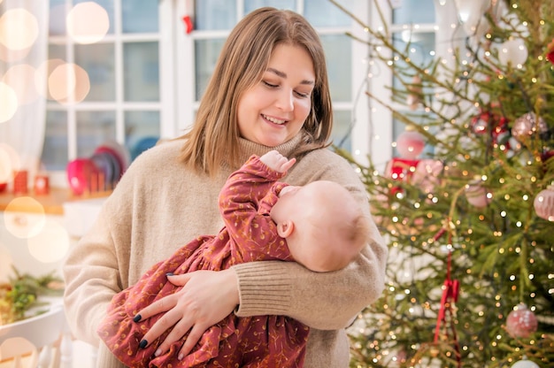 Szczęśliwa mama bawi się z dzieckiem na rękach w domu, a nie na tle udekorowanego pokoju i choinki