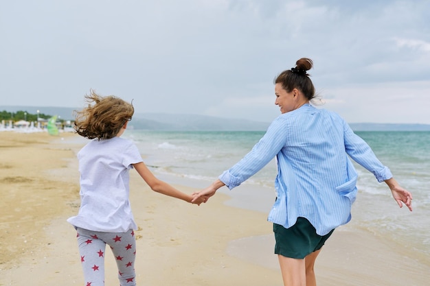 Szczęśliwa Mama I Córka Biegają Po Plaży Trzymając Się Za Ręce Widok Z Tyłu