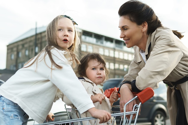 Szczęśliwa mama i jej córki bawią się wózkiem na zakupy