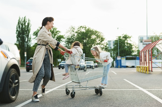 Szczęśliwa mama i jej córki bawią się wózkiem na zakupy