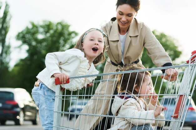 Szczęśliwa mama i jej córki bawią się wózkiem na zakupy