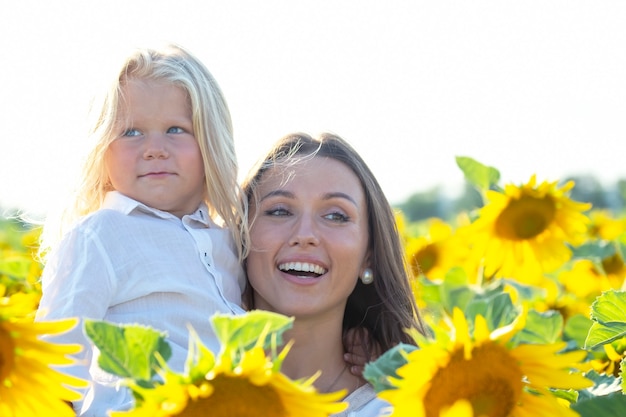 Szczęśliwa mama i uroczy blond syn stoją razem w pobliżu pola słoneczników w świetle słońca