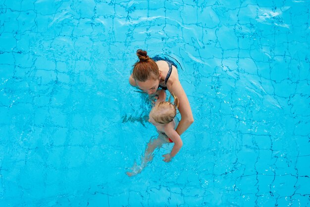 Szczęśliwa mama rodzinna uczy swoją córkę w wieku lat pływać w widoku z góry na basen