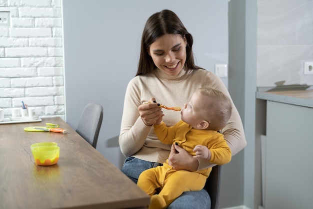 Szczęśliwa mama trzyma dziecko w ramionach. łyżka do karmienia dziecka z synem łyżką w pomieszczeniu. Skopiuj miejsce.