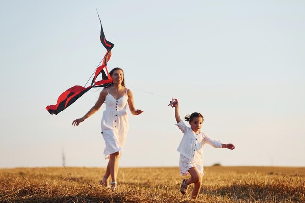 Szczęśliwa mama z córeczką bawią się latawcem na świeżym powietrzu na boisku