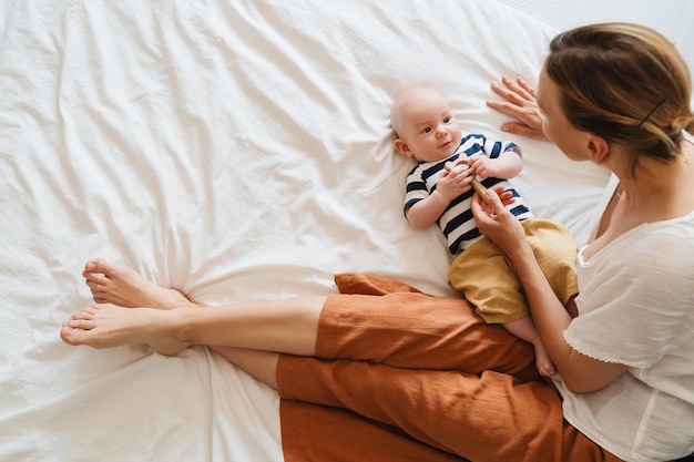 Szczęśliwa matka i dziecko odpoczywają na białym łóżku kochająca matka bawiąca się z dzieckiem w domu