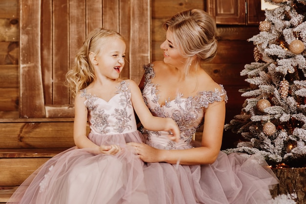 Szczęśliwa Matka i jej córka w różowych sukienkach w pobliżu ozdób choinkowych