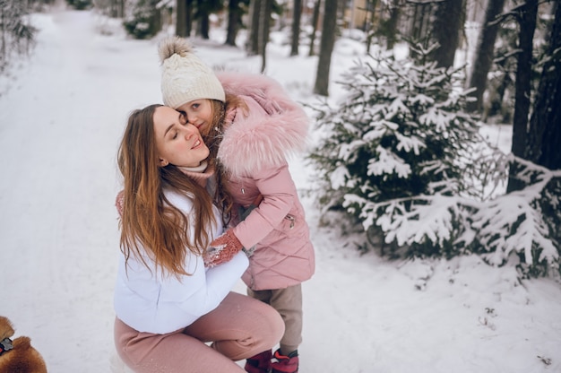 Szczęśliwa matka i mała śliczna dziewczyna w różowej ciepłej odzieży wierzchniej, chodzenie, zabawę i przytulanie w śnieżnobiałej