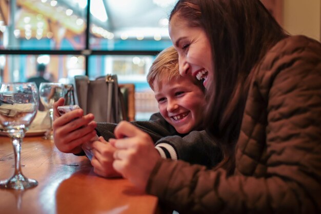 Zdjęcie szczęśliwa matka i syn patrzą na telefon komórkowy w restauracji