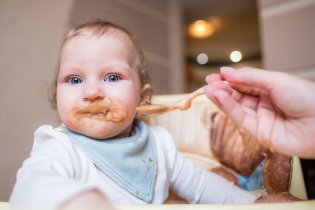 Szczęśliwa matka karmi swoją uroczą małą córeczkę puree owocowym z łyżki w domu Pierwsze jedzenie