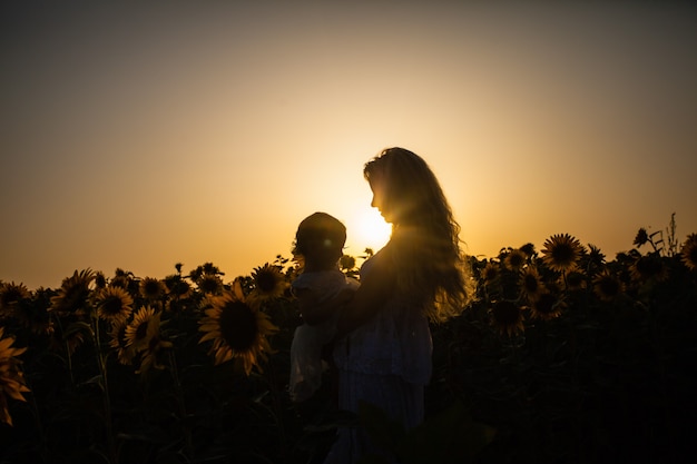 Szczęśliwa matka przytula córkę na polu słoneczników, białe ubrania