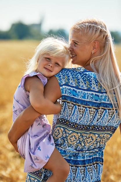 Szczęśliwa matka trzyma dziecko uśmiecha się na polu pszenicy w słońcu.