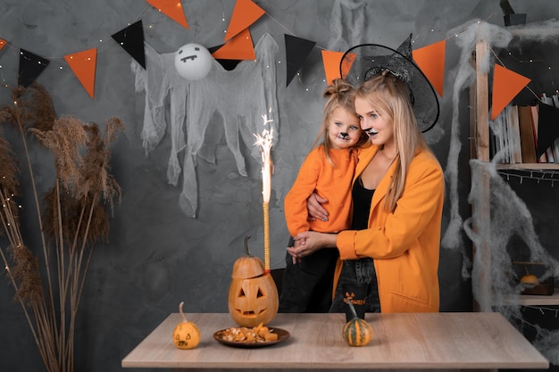 Zdjęcie szczęśliwa matka z córką w kapeluszach na halloween patrzy na pomarańczowe fajerwerki z dyni na imprezę w urządzonym pokoju tradycyjne jesienne wakacje koncepcja halloween