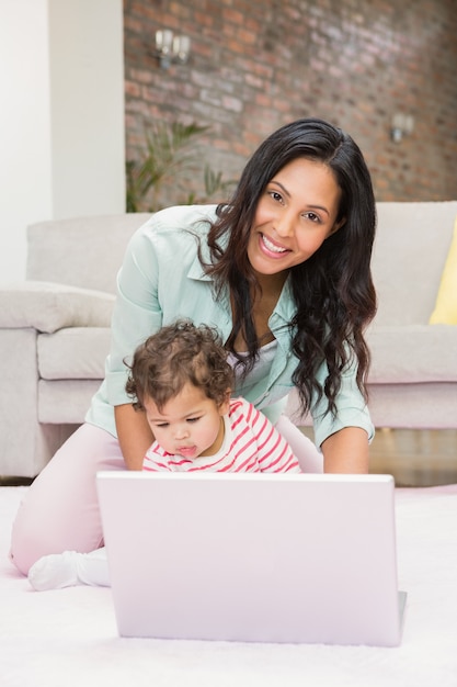 Szczęśliwa matka z jej dzieckiem używa laptop na dywanie w żywym pokoju