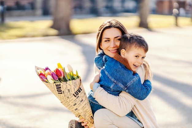 Szczęśliwa matka z kwiatami i synem przytulającym się na dzień matki