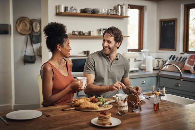 Szczęśliwa międzyrasowa para śniadanie i poranek w kuchni na rozmowę o zdrowym posiłku lub nawiązanie więzi w domu Mężczyzna i kobieta uśmiechają się do rozmowy przy kawie lub herbacie i jedzeniu w weekend razem przy stole
