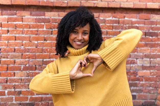 Szczęśliwa młoda African American kobieta co kształt serca rękami przed klatką piersiową. Koncepcja miłości i romansu.