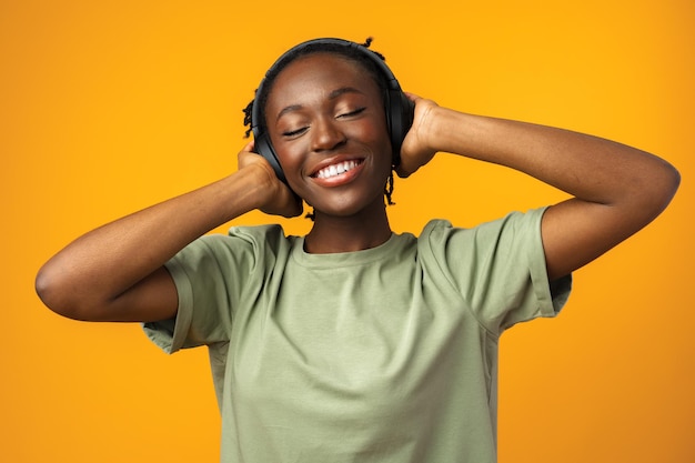 Szczęśliwa młoda afroamerykańska kobieta słuchająca muzyki w słuchawkach na żółtym tle