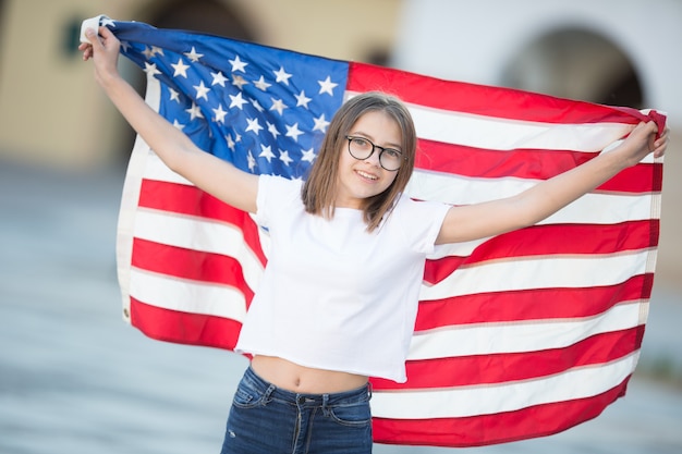 Szczęśliwa młoda amerykańska uczennica trzyma i macha w mieście z flagą USA.