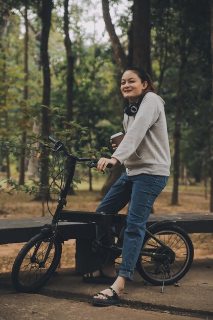 Szczęśliwa młoda Azjatka chodzi i jeździ na rowerze po ulicy Park City uśmiecha się używając roweru transportu przyjaznego dla środowiska Ludzie koncepcja stylu życia