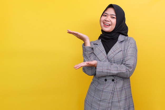 Szczęśliwa młoda Azjatka w hidżabie stojąca na żółtym tle z rękami na t