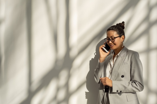Szczęśliwa młoda azjatycka bizneswoman mówiąca przez telefon komórkowy