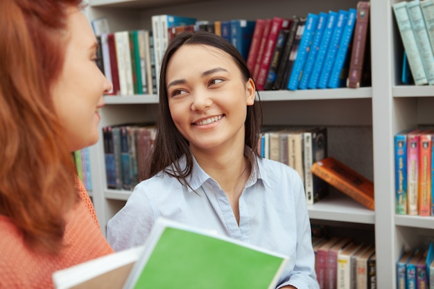 Szczęśliwa młoda Azjatycka kobieta gawędzi jej kolegi kolegium przy biblioteką