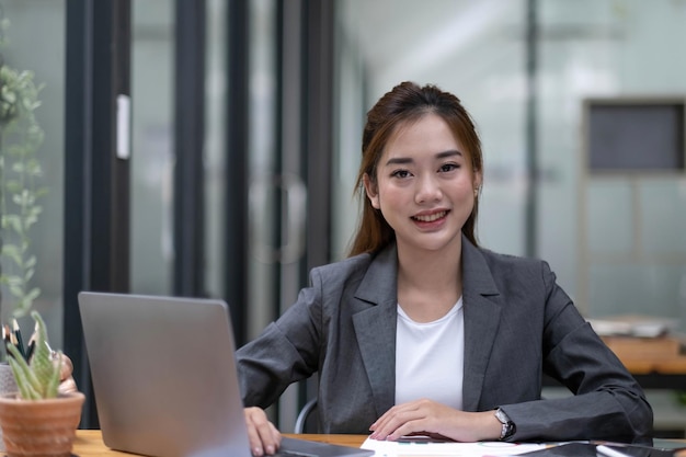 Szczęśliwa Młoda Azjatycka Kobieta Pracująca Na Klawiaturze Laptopa Z Dokumentem W Biurze Patrząc Na Kamerę