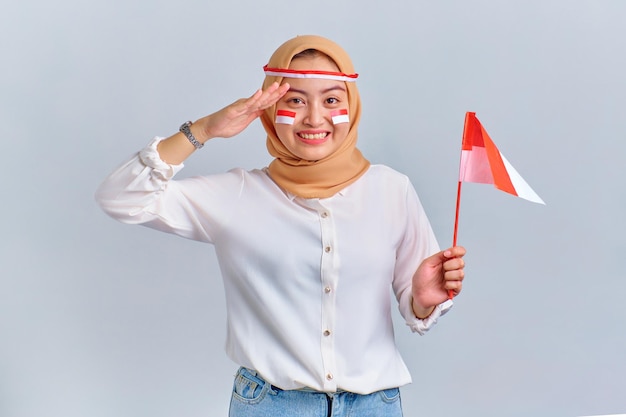 Szczęśliwa młoda Azjatycka kobieta trzymająca indonezyjską flagę i wykonująca gest salutu na białym tle Koncepcja indonezyjskiego dnia niepodległości