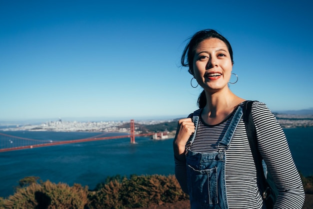 Szczęśliwa młoda azjatycka kobieta turysta śmiejąc się w San Francisco przez most Golden Gate. piękna dziewczyna backpacker odwiedzić słynną atrakcję w przyrodzie california usa. pani zwiedzanie widok miasta miejskiego.