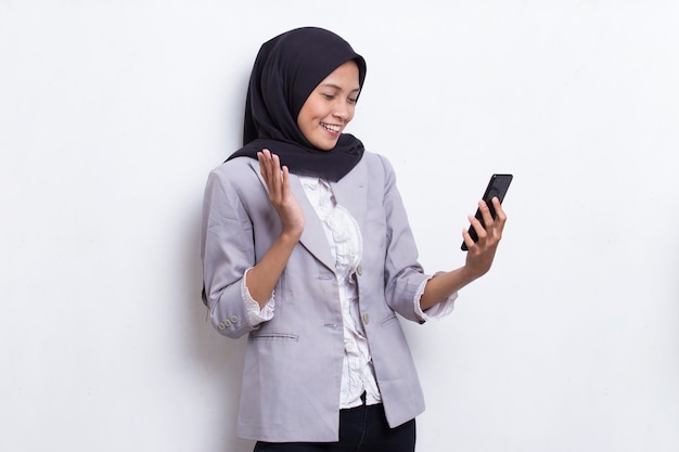 Szczęśliwa młoda azjatycka piękna muzułmańska kobieta korzystająca z telefonu komórkowego na białym tle