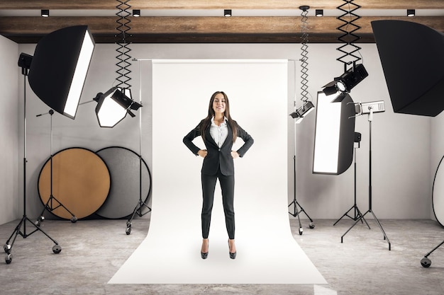 Szczęśliwa młoda bizneswoman stojąca w studiu fotograficznym przy świetle dziennym i profesjonalnym sprzęcie