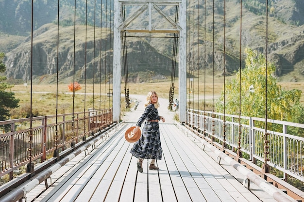 Szczęśliwa młoda blondynka w sukience w kratę na moście Horochowski na rzece Katuń w górach Ałtaj