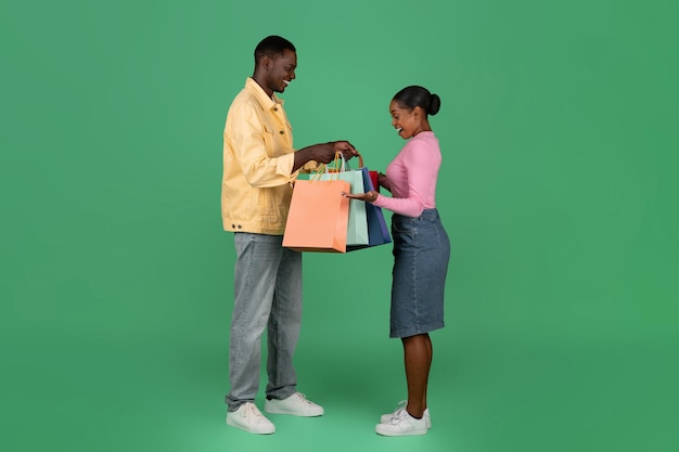 Szczęśliwa młoda czarna kobieta robi zakupy z chłopakiem w papierowych torbach
