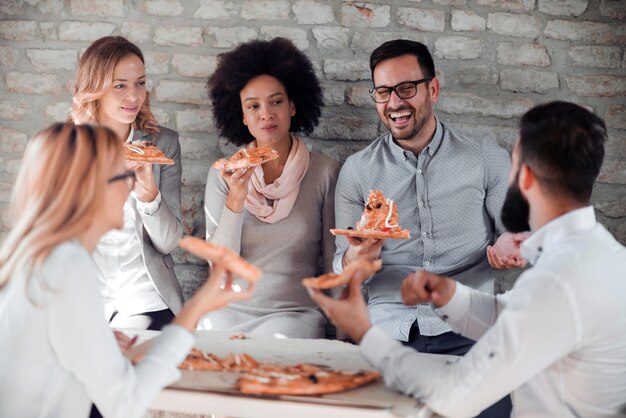 Szczęśliwa młoda drużyna biznesowa jedząca pizzę w biurze