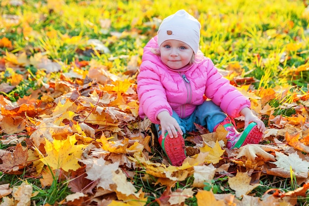 Szczęśliwa młoda dziewczyna gra pod spadającymi żółtymi liśćmi w pięknym jesiennym parku