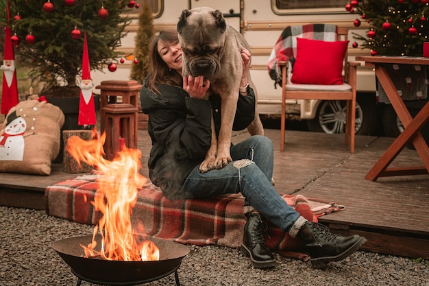 Szczęśliwa młoda dziewczyna i pies spędzają razem czas w święta Bożego Narodzenia Cane Corso i jego kochanka świętują Nowy Rok na łonie natury w pobliżu samochodu kempingowego i przy ognisku