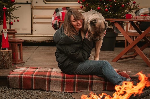 Zdjęcie szczęśliwa młoda dziewczyna i pies spędzają razem czas w święta bożego narodzenia cane corso i jego kochanka świętują nowy rok na łonie natury w pobliżu samochodu kempingowego i przy ognisku