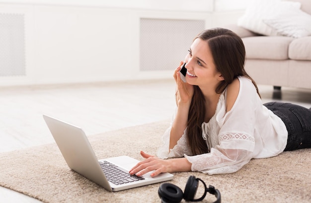 Szczęśliwa młoda dziewczyna na czacie online na laptopie i rozmawiając leżąc na podłodze, z miejsca na kopię. Koncepcja technologii.