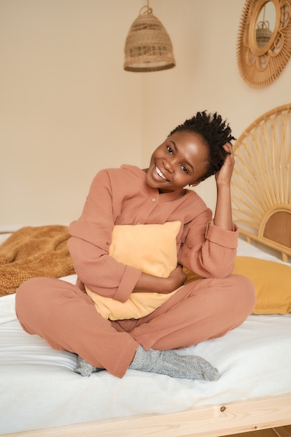 Szczęśliwa młoda dziewczyna siedzi na łóżku w sypialni i używa laptopa muślinowej piżamy na czacie z przyjaciółmi