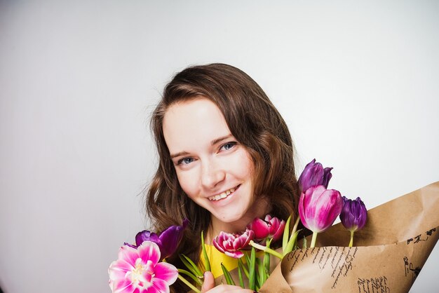 Szczęśliwa młoda dziewczyna trzymająca bukiet pachnących kwiatów, uśmiechnięta, świętująca światowy dzień kobiet