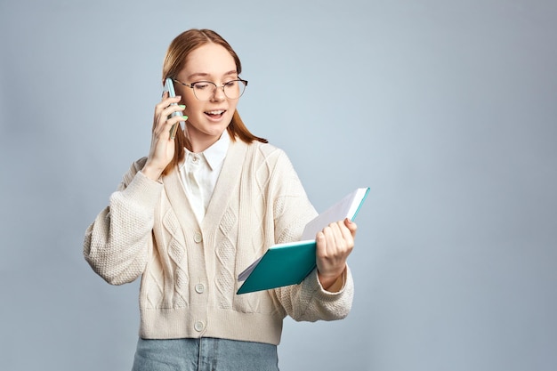 Szczęśliwa młoda dziewczyna ubrana w swobodny sweter rozmawia przez telefon komórkowy podczas czytania notebooka