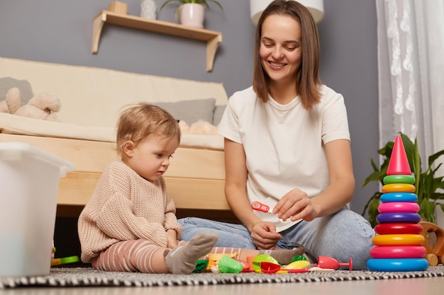 Szczęśliwa młoda kaukaska matka i córeczka bawiące się razem zabawkami w domu uszczęśliwiona mama i małe dziecko uczące się razem siedząc na podłodze