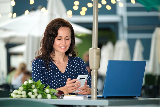 Szczęśliwa młoda kobieta biznesmena siedząca przy stoliku w kawiarni na zewnątrz, pracująca zdalnie na laptopie, tworząc biznes online.