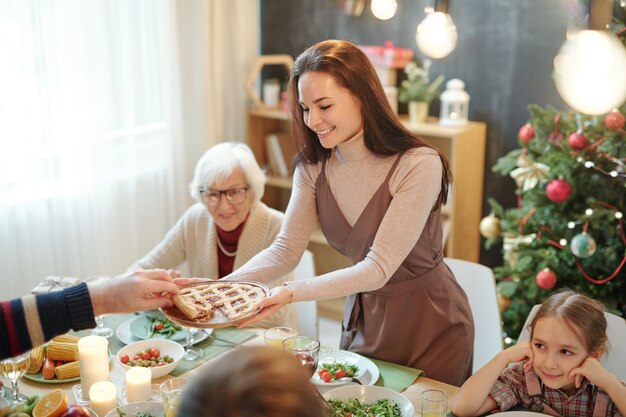 Szczęśliwa młoda kobieta, dając ojcu domowe ciasto przy świątecznym stole podczas rodzinnej kolacji w domu