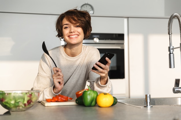 Szczęśliwa młoda kobieta, gotowanie świeżej sałatki w kuchni w domu