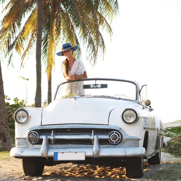 Szczęśliwa młoda kobieta i retro kabriolet przy plaży w mieście Varadero