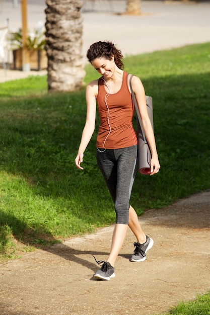 Szczęśliwa młoda kobieta idąca na lekcję jogi w parku