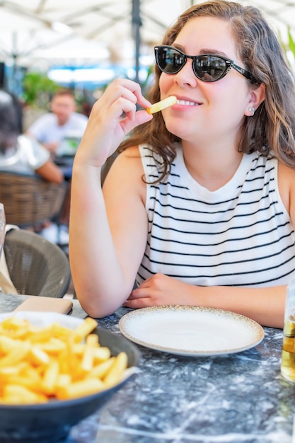 Szczęśliwa młoda kobieta jedząca frytki w restauracji