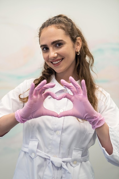 Szczęśliwa młoda kobieta lekarz w mundurze medycznym, pokazując gest lub znak miłości serca